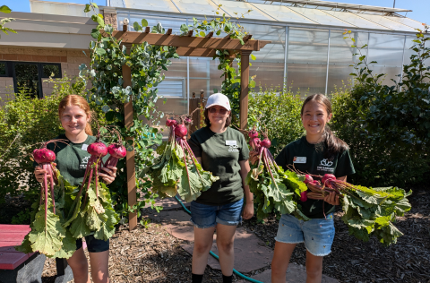 three teens holding vegetables
